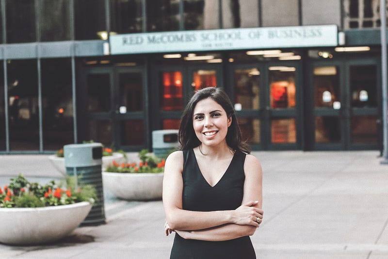 A woman in a black dress crosses her arms in front of the McCombs School of Business