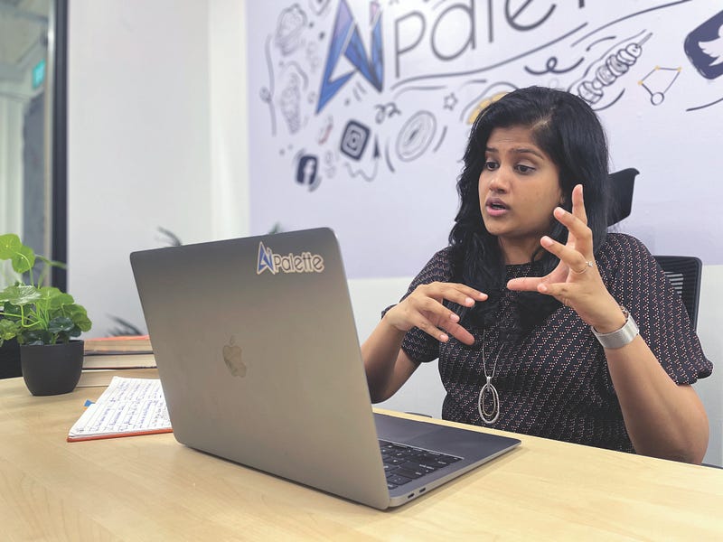 A woman in a navy blouse makes gestures in front of a laptop while talking on a video conference call.
