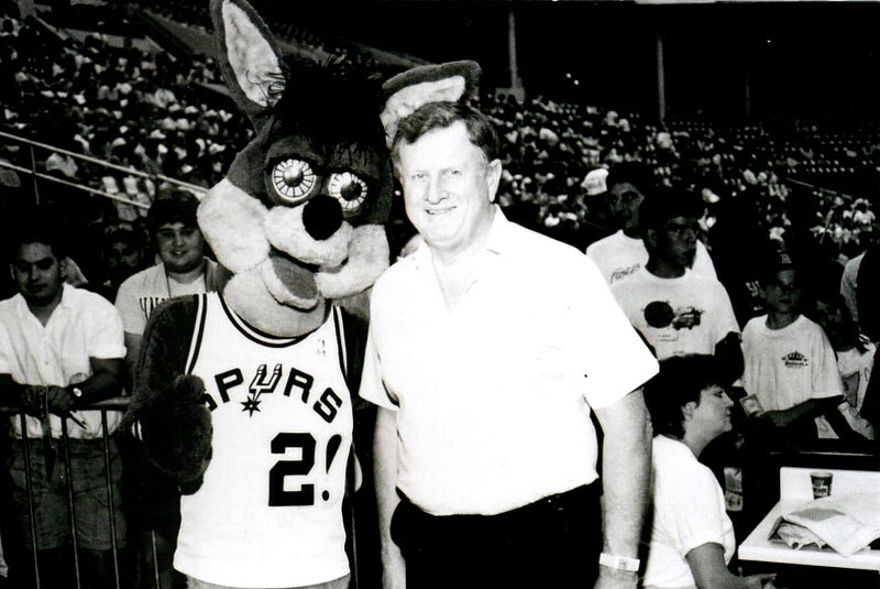 Red McCombs and the San Antonio Spurs mascot in a basketball stadium.