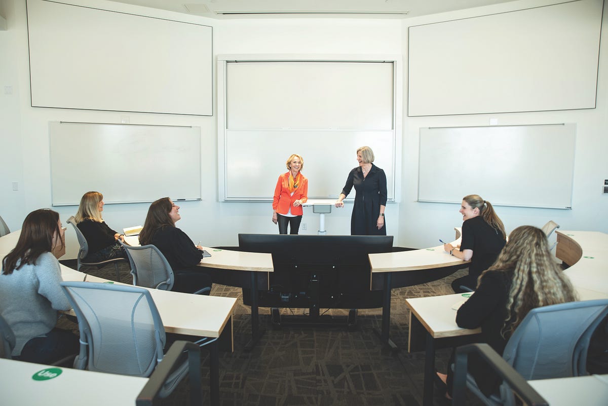 Women sit in a classroom and listen to two women presenting