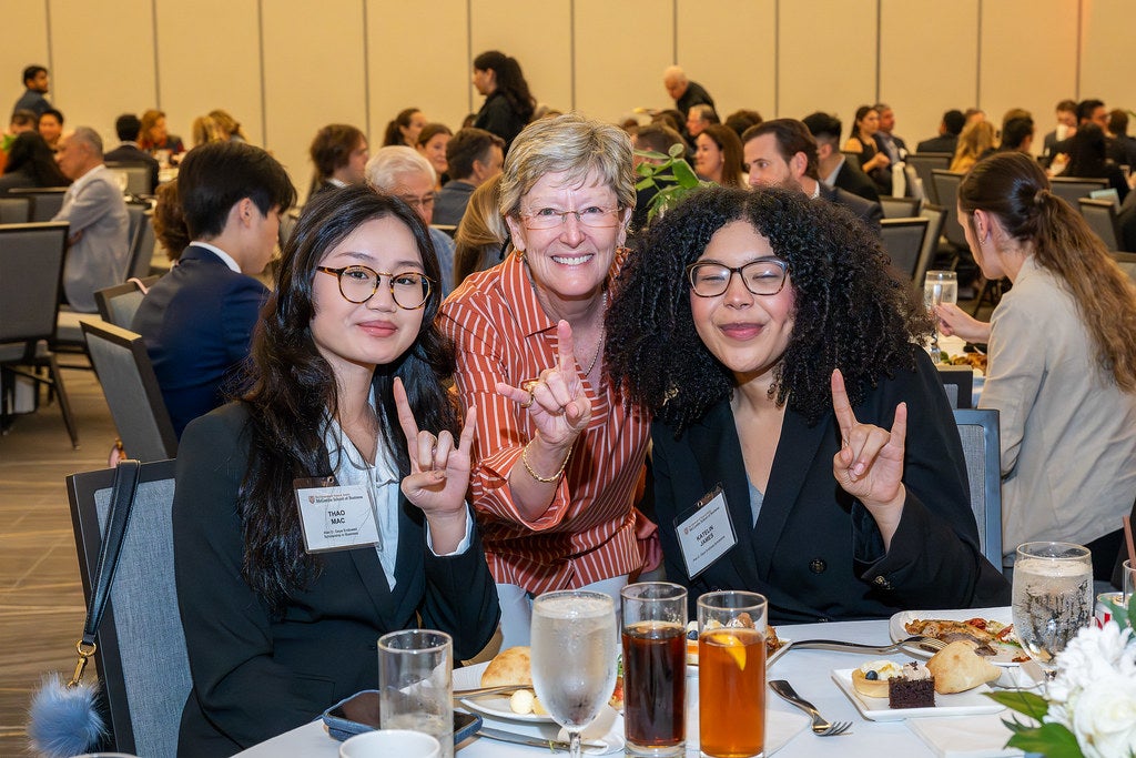 Two students and a scholarship donor smile and flash the "Hook 'Em" hand gesture at the McCombs scholarship luncheon.