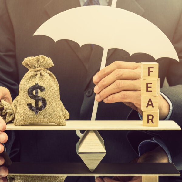 Fear and greed or anxiety in financial market concept : Businessman carries a white umbrella, protects dollar bags or properties on basic balance scale, depicts the influence of emotions on investors